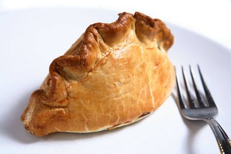 A traditional British Cornish Pasty - a pastry case filled with a thick meat and potato stew - with a fork on a plate.の写真素材