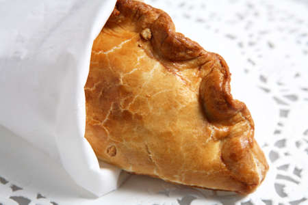 A traditional English Cornish pasty meat pie, wrapped in a tissue and lying on a paper doileyの写真素材