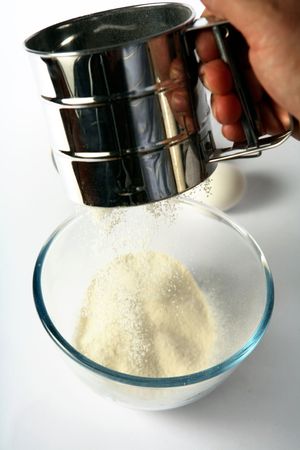 Sifting flour into a glass mixing bowl, with an egg in the background.