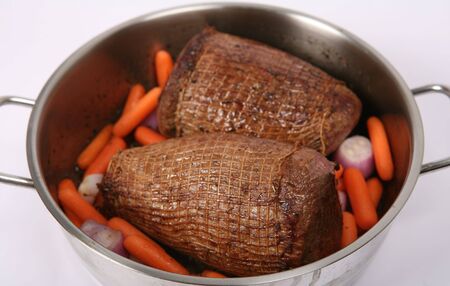 Round beef joints, browned ready for braising (pot-roasting) in a Dutch oven with carrots and shallots.の写真素材