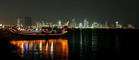 The Doha Corniche at night, with an illuminated pleasure dhow in the foreground and the West Bay...