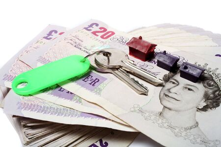 A set of house keys resting on a big pile of used 20 pound notes with some toy houses - perhaps a rent or mortgage payment or deposit... の写真素材