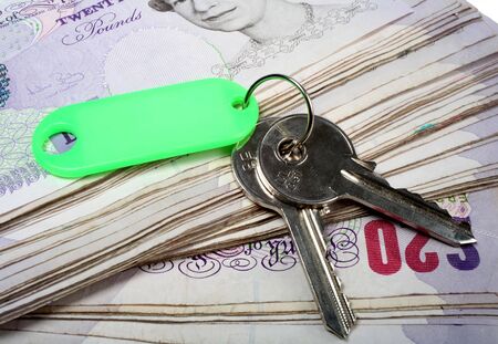 A set of house keys resting on a big pile of used 20 pound notes - perhaps a rent or mortgage payment or deposit... or the keys to successの写真素材