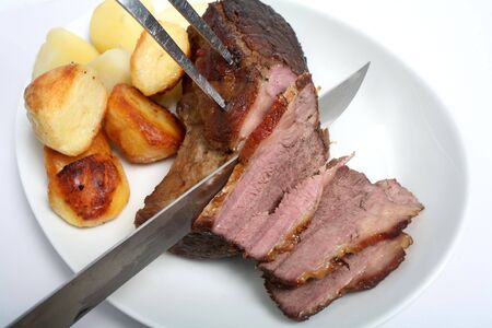 Carving a joint of roast beef on a plate with roasted and boiled potatoes.の写真素材