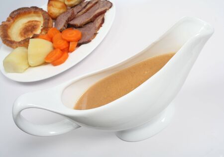 A gravy boat in front of a plate of traditional British Sunday lunch of roast beef and yorkshire puddingの写真素材