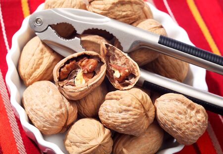 A bowl of walnuts with a pair of nutcrackers, one of the nuts broken open