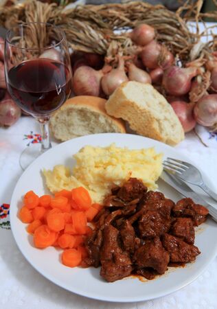 A rustic meal of traditional French boeuf bourguignonne beef stew, with red wine and bread and a string of onions in the backgroundの写真素材