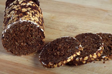 A traditionally tin-cooked pumpernickel rye bread loaf sliced on a chopping board