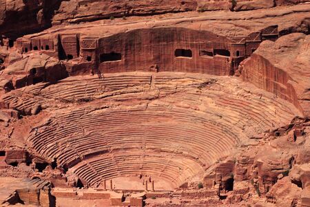 An aerial view of the Roman-era amphitheater carved into the pink sandstone at Petra, Jordan. The building facades cut into the rock behind are ancient graves.の写真素材