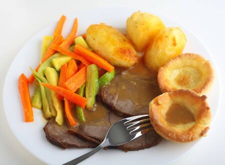 Close-up, slanted view of slices of roast beef with yorkshire pudding, roasted potatoes and sauteed carrots and courgettes, topped with a rich gravyの写真素材