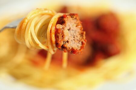 A meatball with tomato sauce and spaghetti on a fork, with the plate in the background.の写真素材