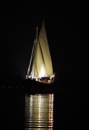 An Arab dhow with its lateen sail lit up in West Bay, Doha, Qatarの写真素材