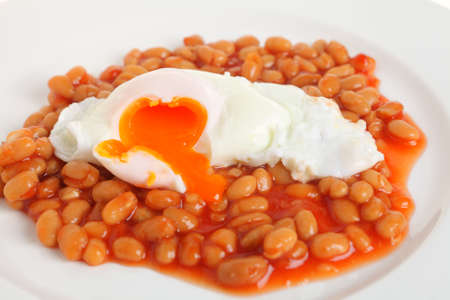 A meal of poached egg on baked beans in tomato sauce, on a white plate.の写真素材