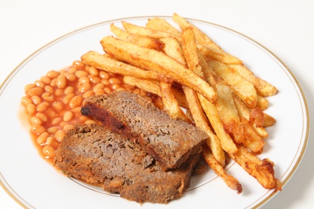 A plate of meatloaf served with baked beans and chips or french fries.
