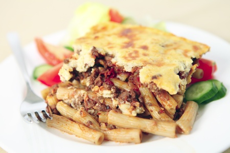 Plate of pastitsio meat and pasta topped with bechamel sauce and cheese, with tomato, cucumber and lettuce. Selective shallow depth of fieldの写真素材