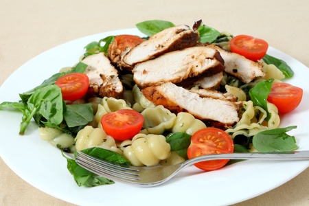 Grilled chicken breast slices served on a bed of pasta shells, garnished with tomato and fresh basilの写真素材