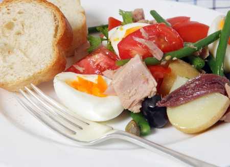 A meal of traditional nicoise salad - lettuce, potato, tomato, green beans, tuna, anchovies, boiled eggs, capers, black olives and a garlic vinegrette and garnished with flat-leaf parsley - served with slices of French breadの写真素材