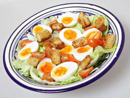 A bowl of salad with hard-boiled eggs, miniature plum tomatoes, iceburg lettuce and homemade...