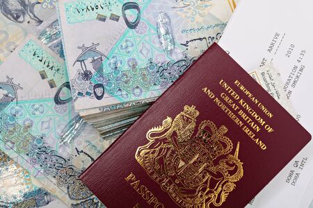A new British passport with a booking form for a flight to Doha, Qatar, and a boarding pass on top of tens of thousands of Qatari riyals  A business opportunity or money to lure expat workers to the Gulf state, perhapsの写真素材