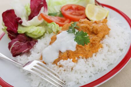 Chicken tikka masala topped with fresh yoghurt on a bed of basmati rice, all served with a fresh saladの写真素材