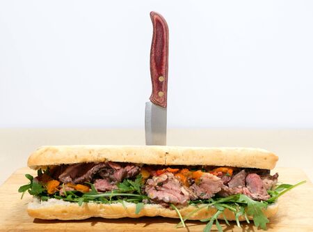 A ciabatta loaf filled with rocket  aragula , pan-seared beef, and pickled sweet peppers, pinned together with a knifeの写真素材