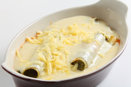 An oven bowl with stuffed cannelloni topped with bechamel sauce and a sprinkling of cheese, ready for baking.の写真素材