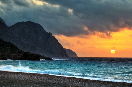 The sun dips below threatening clouds at sunset in Sougia, a small and fairly inaccessible town on the south coast of Crete, Greece   Cut off from neighbouring areas by the soaring mountains of Sfakia, Sougiaの写真素材