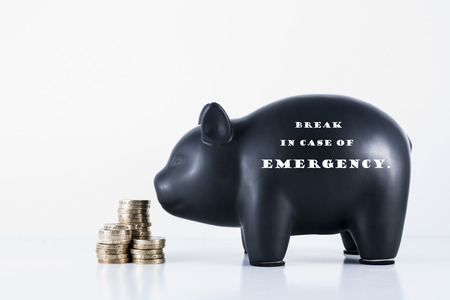 Black piggy bank and some coins with the motif - Break in case of Emergencyの写真素材