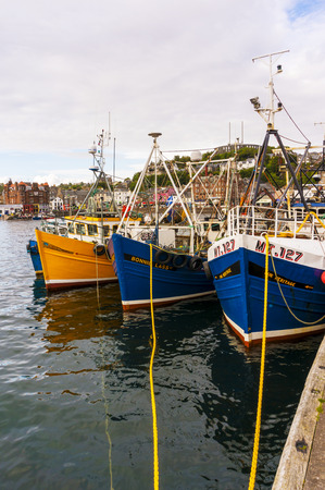 Oban Harbour, Oban, Argyle, Scotland. 28th August 2015. A typical scene in Oban harbour with the fishing boats moored, the harbourside shops behind and McCaigs folly on the hillside. In portrait format.のeditorial素材