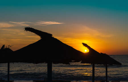 Beautiful background image for summer vacation at sunrise with silhouette natural umbrellas on the beach.の写真素材