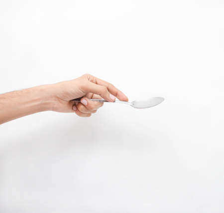A person's hand holding a metal spoon on an isolated white backgroundの写真素材