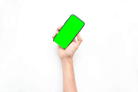 Hand of a young man holding a cell phone isolated on a white background with a green color screen