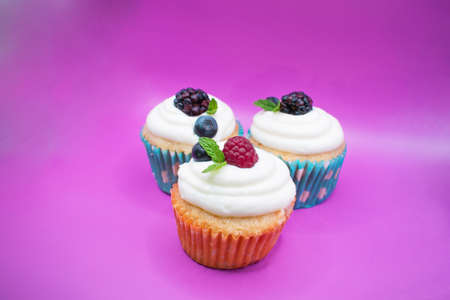 Cupcakes decorated with fresh berries and mint on a purple backgroundの写真素材