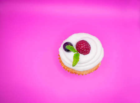 Cupcake with raspberry and mint on a pink background. Top view.