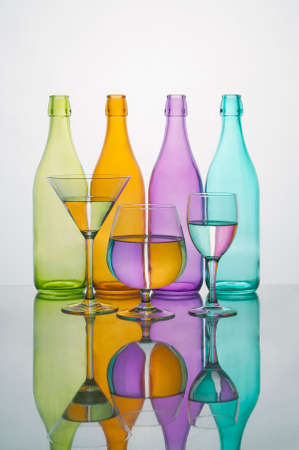 Colored glass bottles with glasses with water colored reflections. Reflected on a mirror on a white backgroundの写真素材