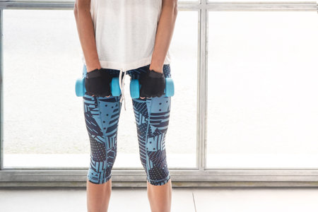 Close up of a light blue dumbbell in the gym and a young woman legs doing workour on a whithe background. Horizontalの写真素材