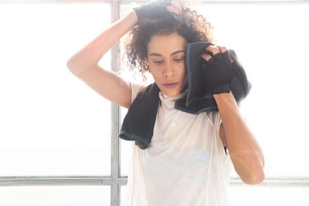 Close up of a young and beautiful woman drying sweat with a towel after workout in a gym horizontalの写真素材