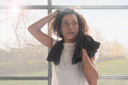 Close up of a young and beautiful woman drying sweat with a towel after workout in a gym with trees background horizontalの写真素材