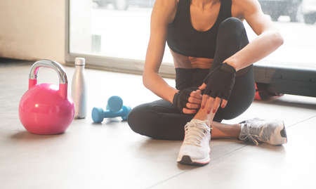 Close up of a light blue dumbbell on the floor of a gym with a pink kettlebell a silver bottle of water and a young woman sitting down horizontalの写真素材