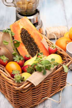 Basket of tropical fruits, oranges, pears kiwi papaya with a mixer on a wodden table. Verticalの写真素材