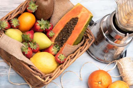 Basket of tropical fruits, oranges, pears kiwi papaya with a mixer on a wooden table. horizontalの写真素材