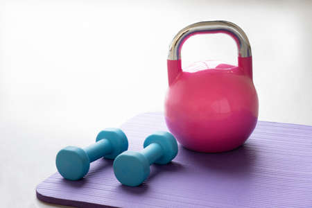 Close up of a blue light weights on a violet yoga pilates mat on the floor of a gym with a pink kettlebellの写真素材