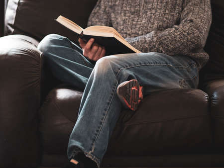 man sits on sofa reading a book casually dressed in blue jeans and sweater