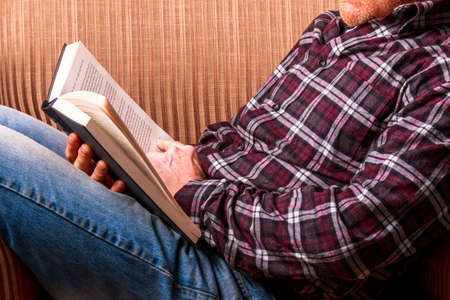Man sat in a chair reading a book blue jeans and a check shirt casually dressedの写真素材