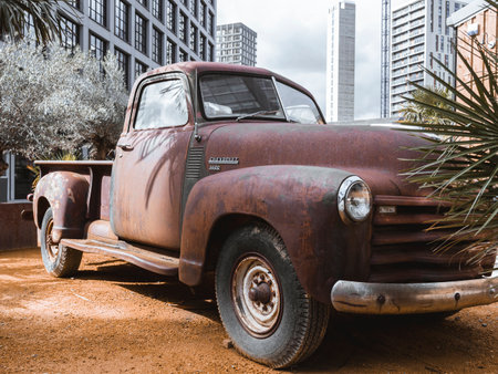 Manchester, UK, September 28, 2024: A rusty vintage truck parked amidst urban high-rise buildings and palm trees.のeditorial素材
