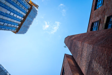 A modern glass building and a historical brick structure stand against a vibrant blue sky. The image captures the architectural contrast between modern and old.の写真素材