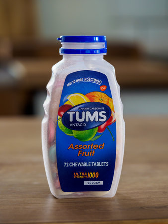 Swinton, Greater Manchester, UK. December 24, 2024: A bottle of assorted fruit antacid chewable tablets on a wooden table.のeditorial素材