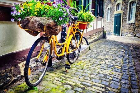 Old rusty bicycle with flowers leaning against house wall