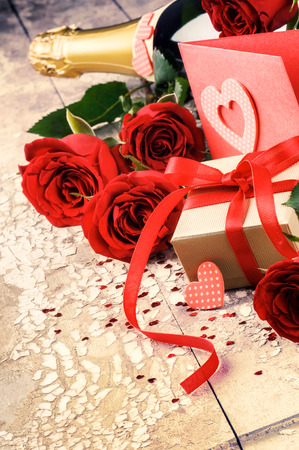 Valentine's setting with present, red roses and bottle of champagneの写真素材