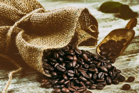 Roasted coffee beans pouring from burlap sack on old wooden table. Close upの写真素材